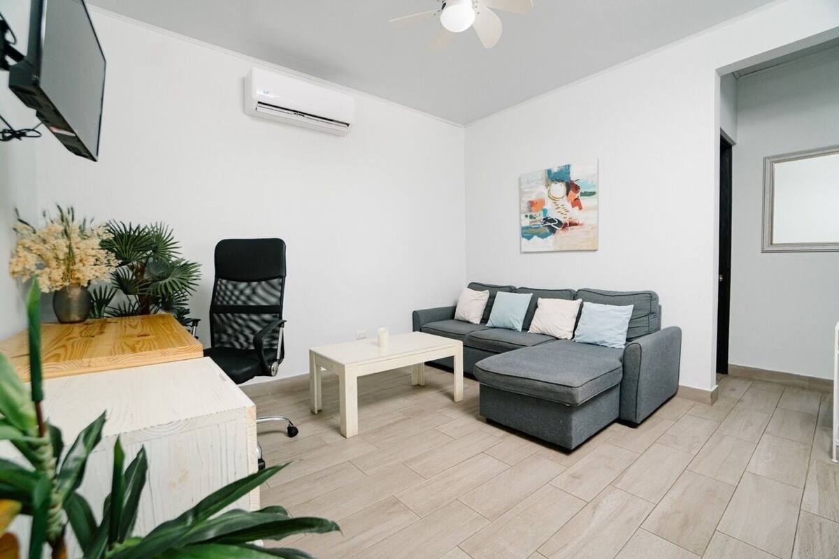 A modern living room with a grey sectional sofa, a white coffee table, a black office chair, and a potted plant.