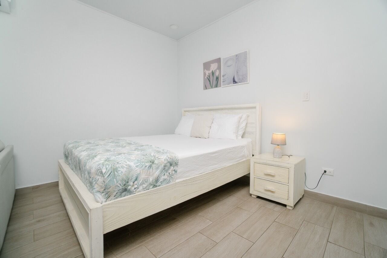 A bedroom with a single bed, a bedside table with a lamp, and a nightstand.