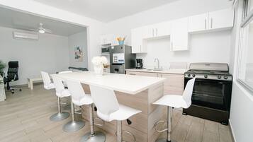 Een moderne keuken met een centraal eiland, witte barkrukken, een zwarte oven en witte kasten.