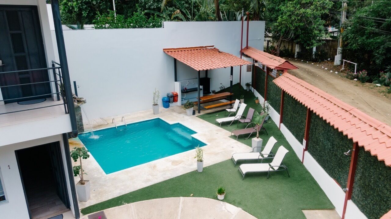 A rooftop pool area with a rectangular pool, lounge chairs, and a pergola with a red roof.