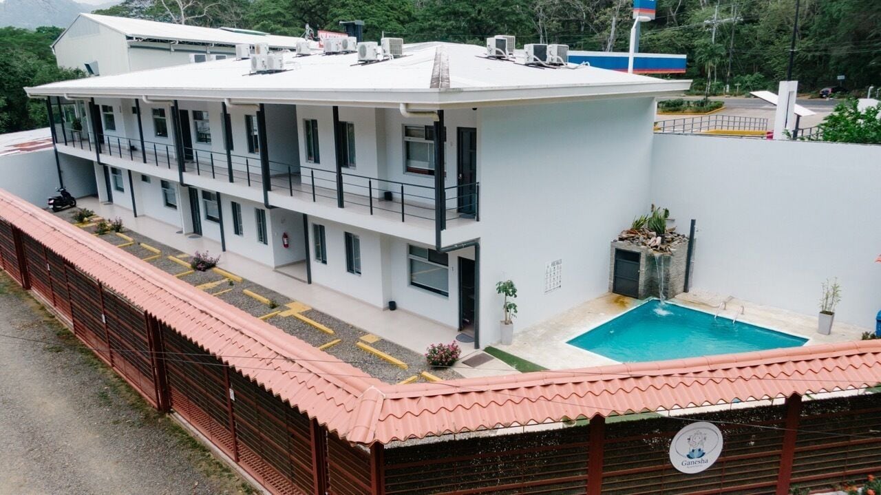 A modern building with a rooftop pool, multiple balconies, and a gated entrance.