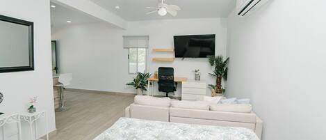 A modern bedroom with a bed, a desk, a chair, a TV, and a ceiling fan.