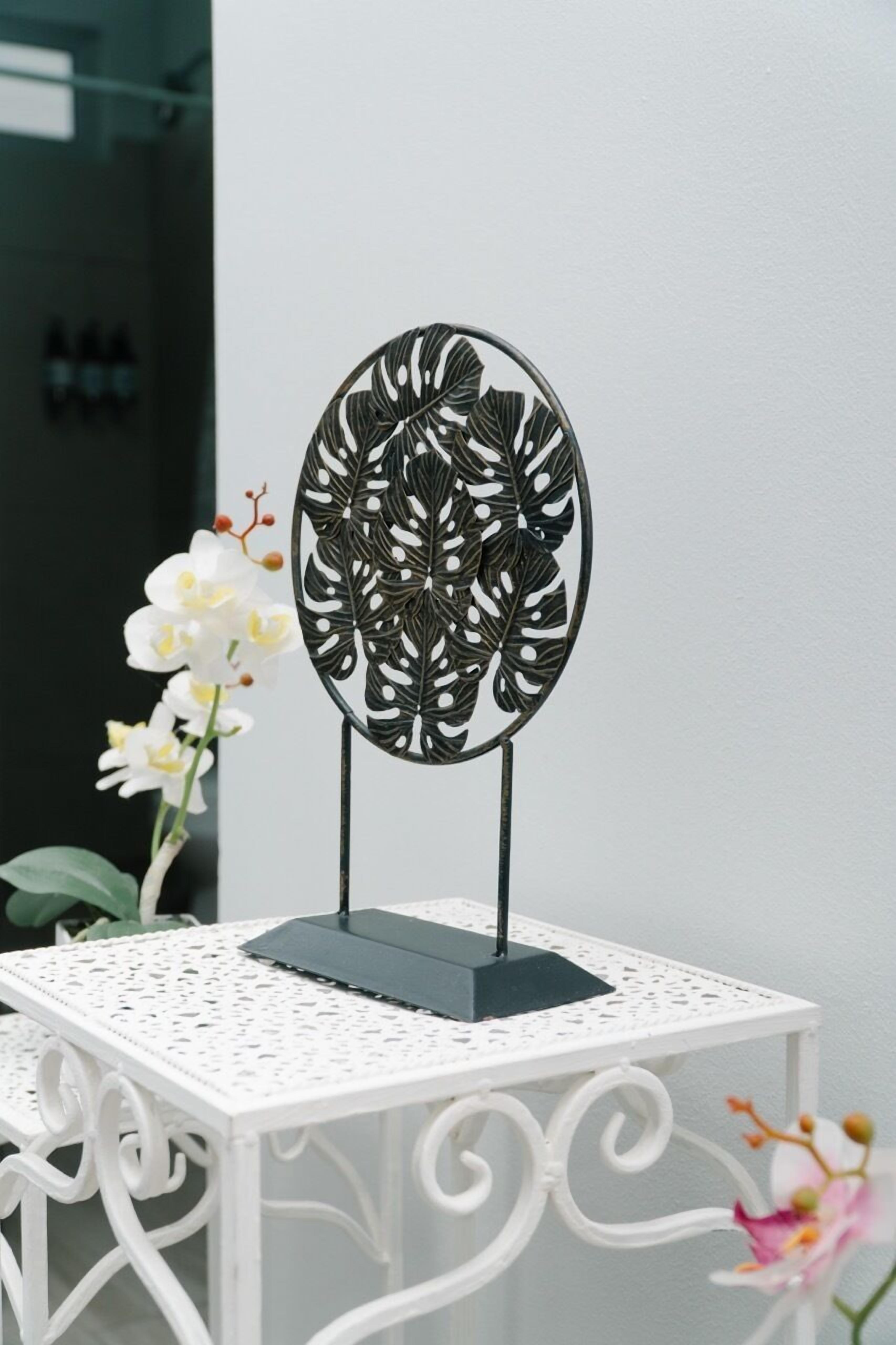 A white table with a decorative metal stand featuring a leaf pattern, accompanied by white orchids.