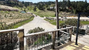 Une vue depuis un balcon donnant sur une route, avec une clôture en bois, une horloge et un espace verdoyant planté d’arbres.