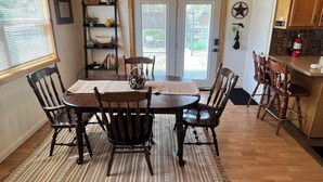 Un coin repas avec une table et des chaises en bois, un ventilateur de plafond et une vue à travers les portes vitrées.