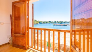 Una habitación con puerta de madera, un balcón con barandilla de madera y vista a un cuerpo de agua con barcos.