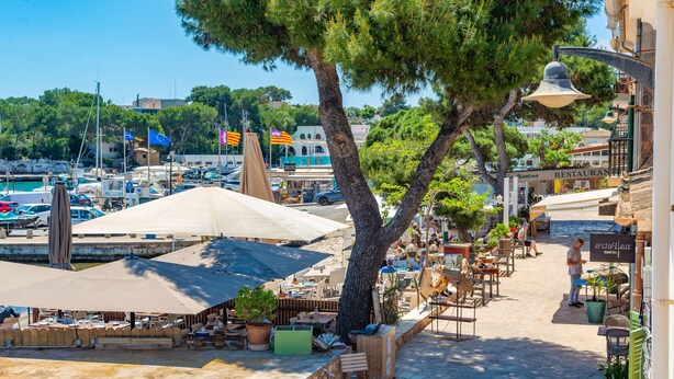 Un café frente al mar con terraza, vistas al puerto deportivo y un restaurante al fondo.