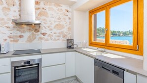 Una cocina moderna con armarios blancos, un horno Bosch, una cafetera y vistas al mar a través de un ventanal grande.