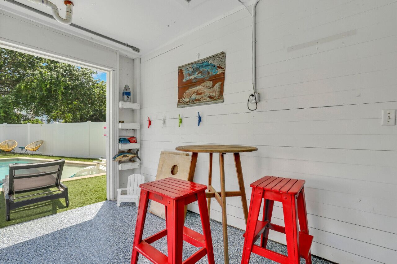 Une pièce avec une piscine, des tabourets rouges, une table en bois et un tableau au mur.
