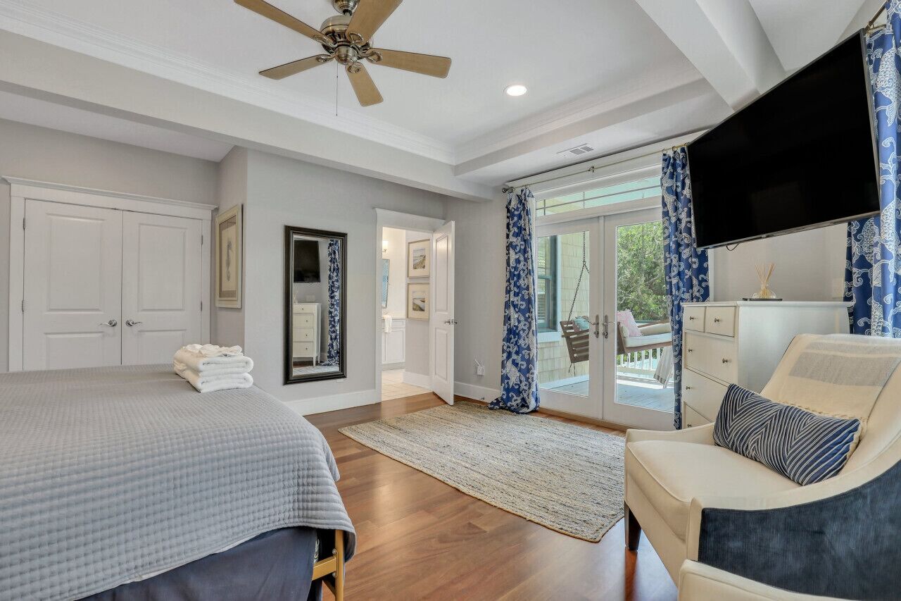 A bedroom with a bed, a chair, a television, and a view of the outdoors.