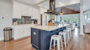A modern kitchen with white cabinetry, a large island, and a bar area with stools. - Tybee Skies: 4 BDR 4 Bath Oceanfront Home w Pool (Tybee Island)