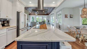 A modern kitchen with a large island, white cabinetry, and a stainless steel range hood. - Tybee Skies: 4 BDR 4 Bath Oceanfront Home w Pool (Tybee Island)
