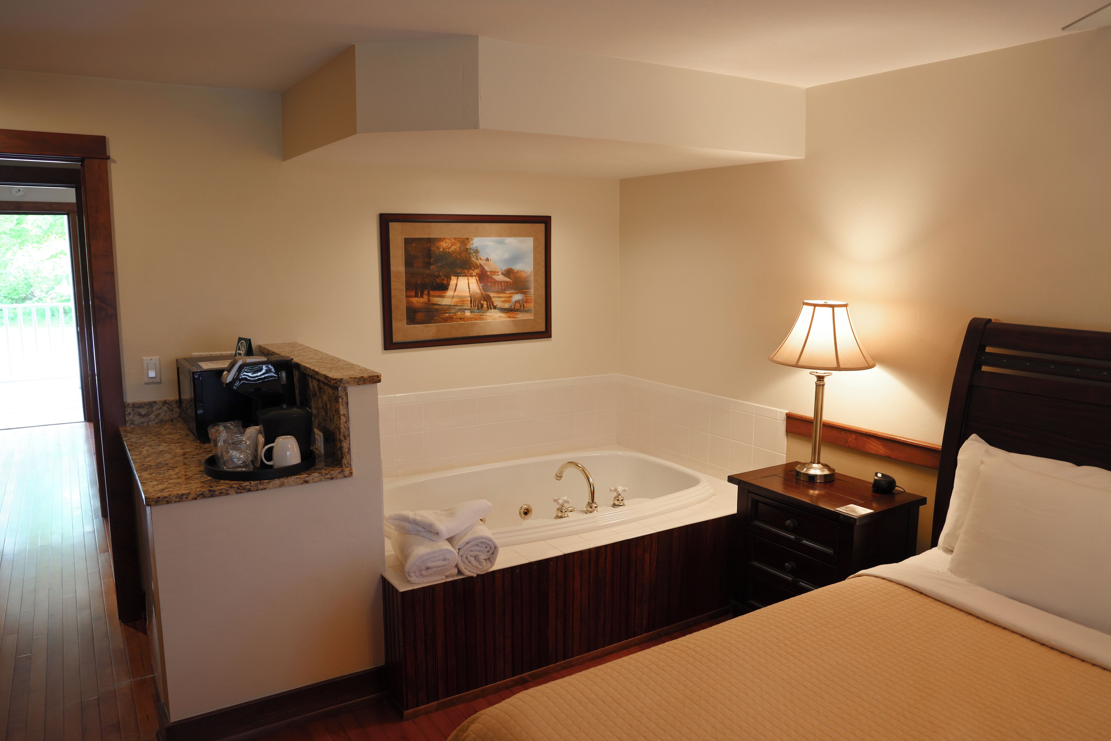 Habitación de hotel con una cama grande, baño con bañera, un cuadro en la pared y una mesita de noche con lámpara.