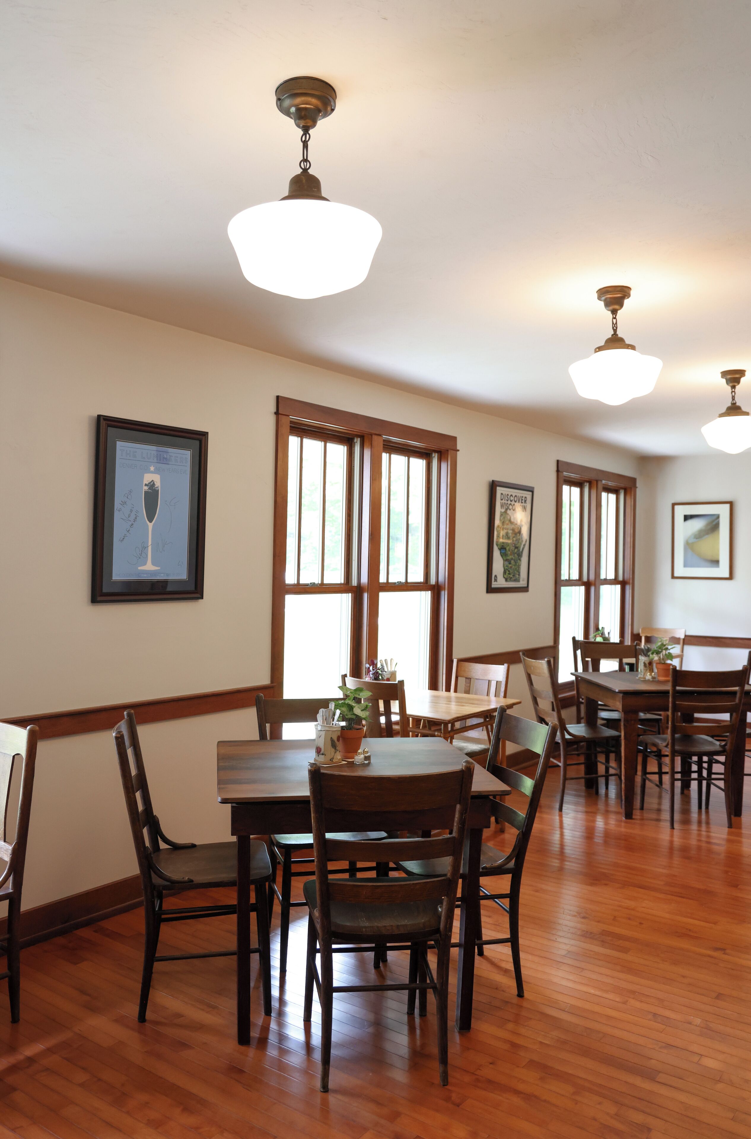 A dining area with wooden tables and chairs, large windows, and ceiling lights.