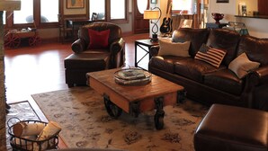 Ein großzügiges Wohnzimmer mit Kamin, Ledersofas, einem Couchtisch und großen Fenstern.
