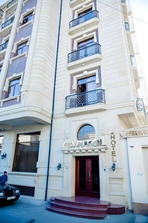 Entrada de un hotel con fachada curva, varios balcones y un llamativo letrero que dice 'CAFITOL HOTEL'.