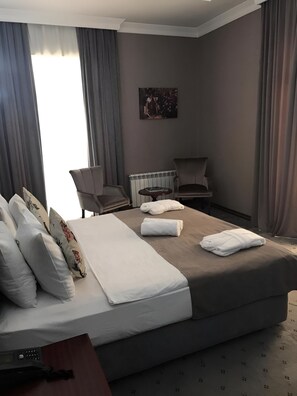 A hotel room with a bed, a chair, a table, and a radiator. - Capitol Hotel (Baku)