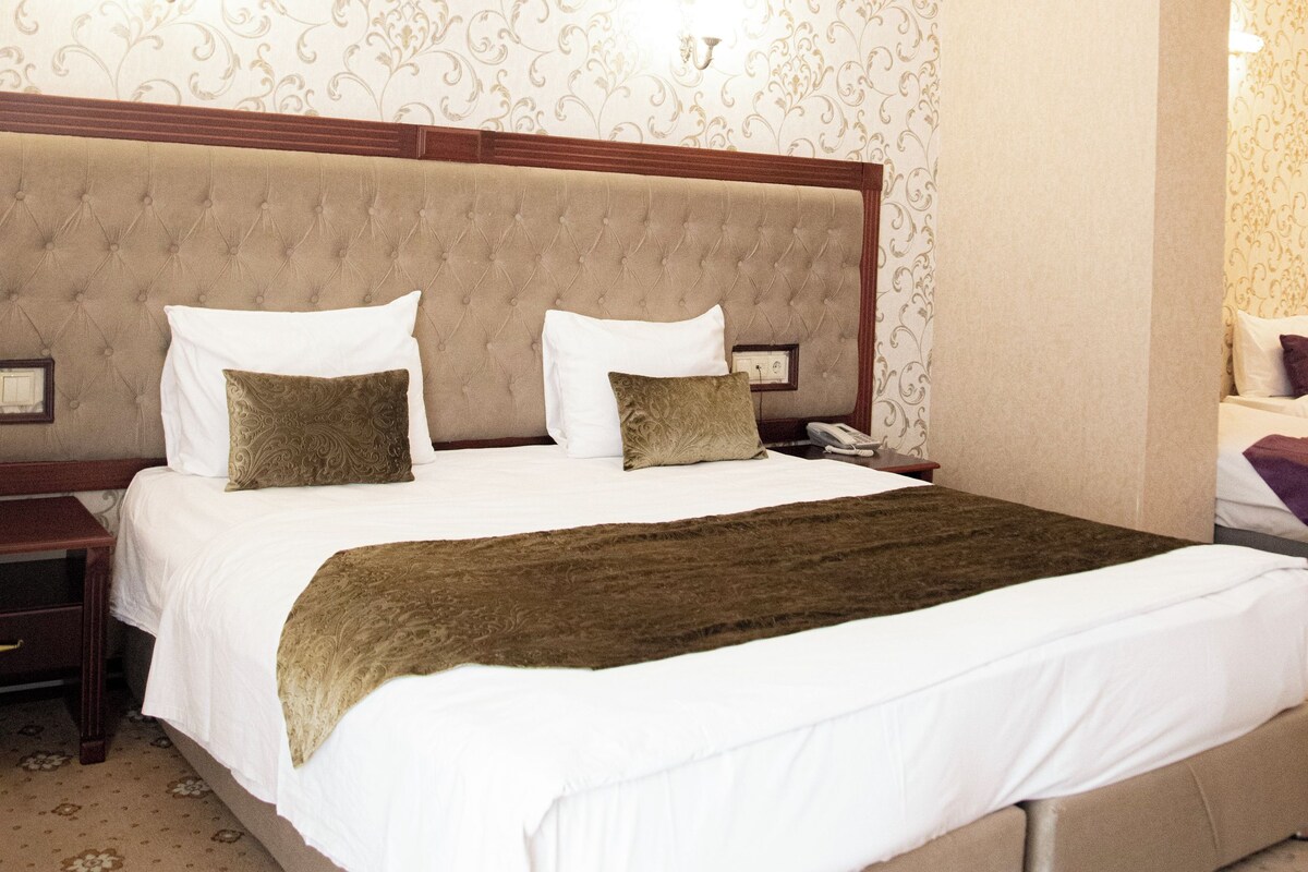 A hotel room with a large bed, a nightstand, and a wall-mounted lamp.
