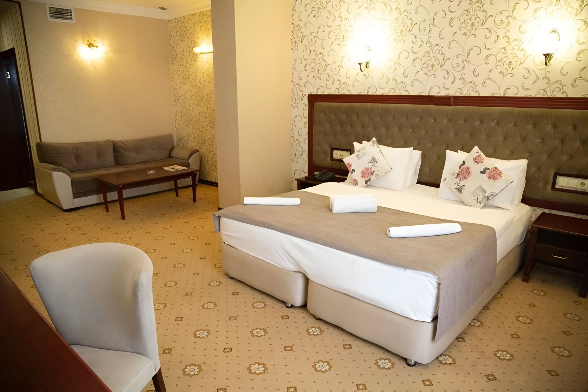 A hotel room with a large bed, a sofa, a chair, and two bedside tables.