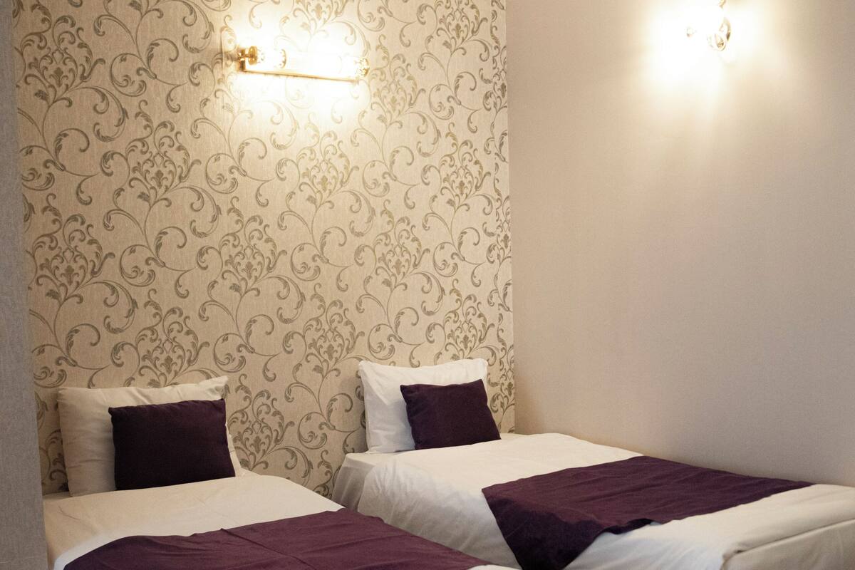 A hotel room with two beds, patterned wallpaper, and wall-mounted lights.