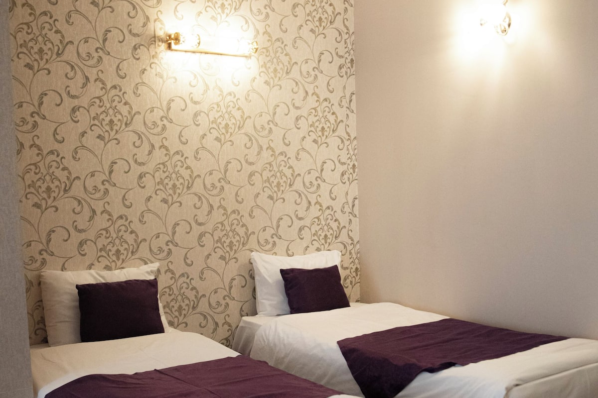 Ett hotellrum med två sängar, mönstrat tapet och väggmonterade lampor.