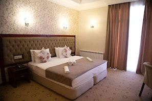 A hotel room with a large bed, a nightstand, a chair, and a radiator. - Capitol Hotel (Baku)