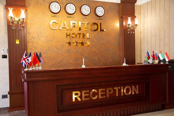 A reception desk at the Capitol Hotel with clocks, flags, and a 'RECEPTION' sign. - Capitol Hotel (Baku)