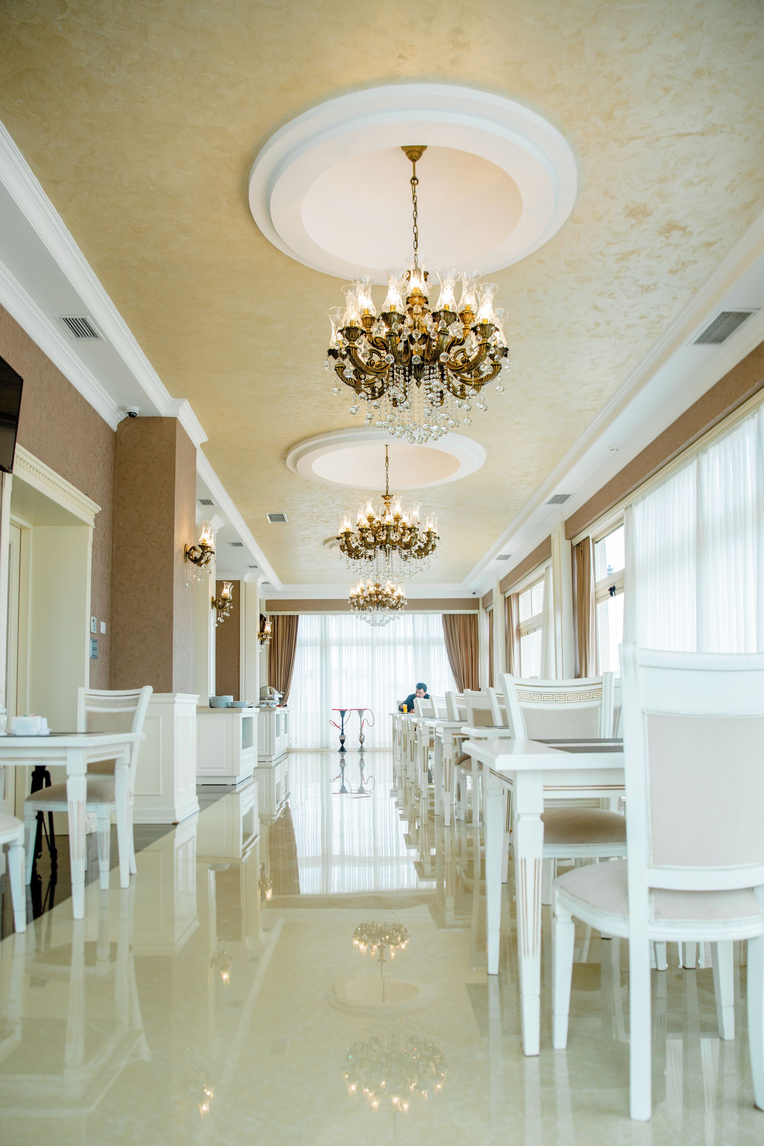 A spacious hotel lobby with a high ceiling, ornate chandeliers, and a long row of white chairs.