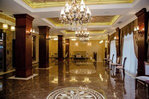 Vestíbulo de hotel con candelabro, suelo de mármol y filas de sillas.