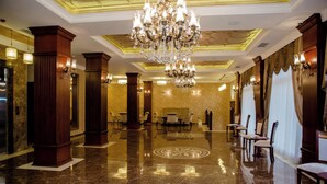 A hotel lobby with a chandelier, marble floor, and rows of chairs.