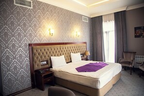 A hotel room with a large bed, two bedside lamps, a nightstand, a chair, and a window with curtains. - Capitol Hotel (Baku)