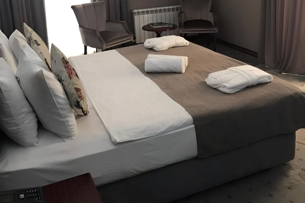 A hotel room with a bed, a chair, a table, and a radiator.