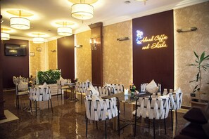 A restaurant with a marble floor, white chairs, and a neon sign reading "Almad Coffee and Shisha". - Capitol Hotel (Baku)