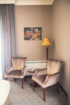 Habitación de hotel con dos sillones, un radiador, una lámpara y una pintura de paisaje urbano en la pared.