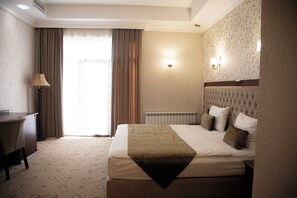 A hotel room with a bed, a desk, a lamp, and a radiator. - Capitol Hotel (Baku)