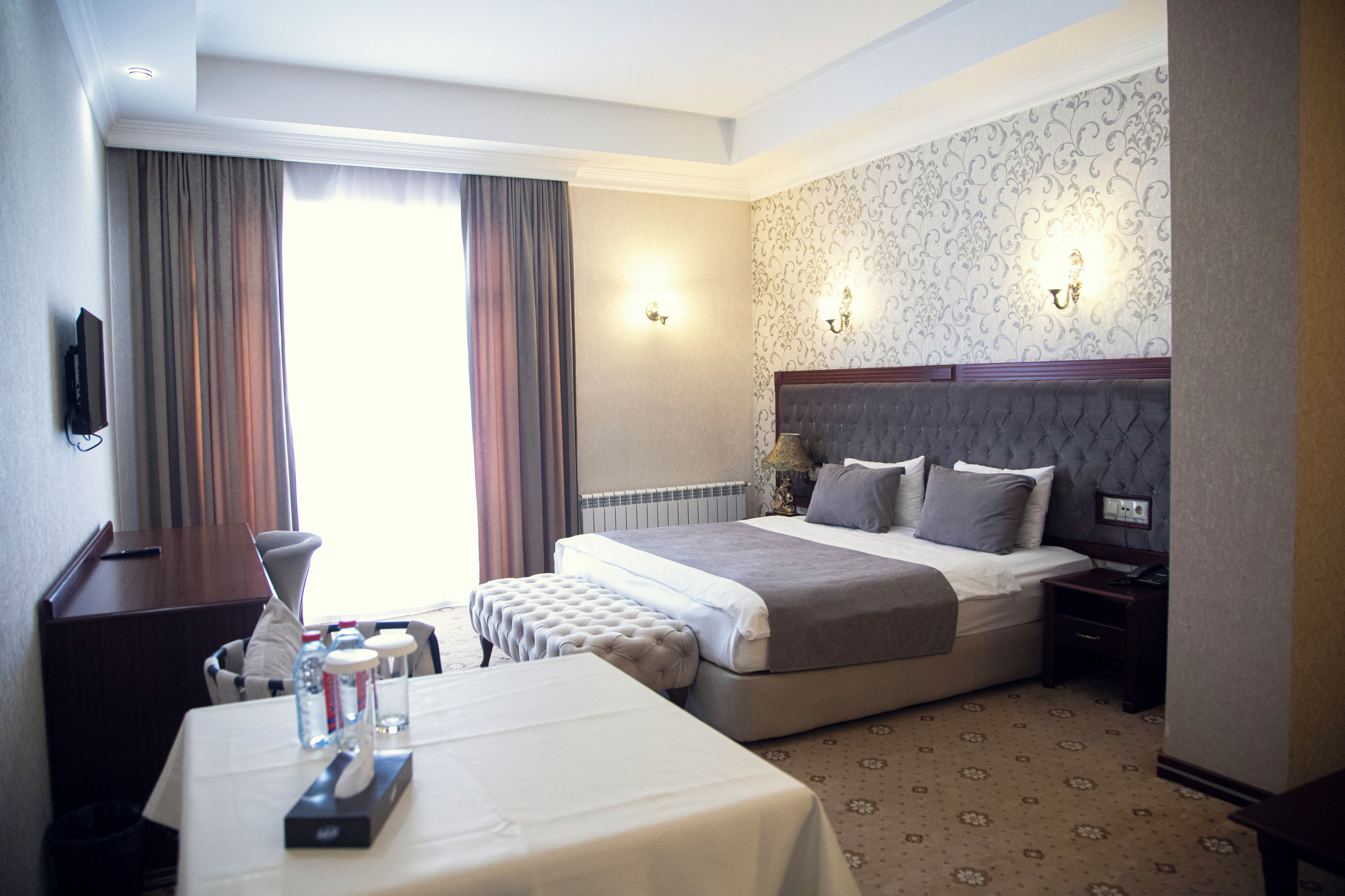 A hotel room with a large bed, a bedside table, a chair, a desk, and a TV.