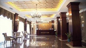 A hotel reception area with a polished marble floor, a chandelier, and a reception desk with flags.