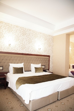 A hotel room with a large bed, a nightstand, and a wall-mounted lamp. - Capitol Hotel (Baku)