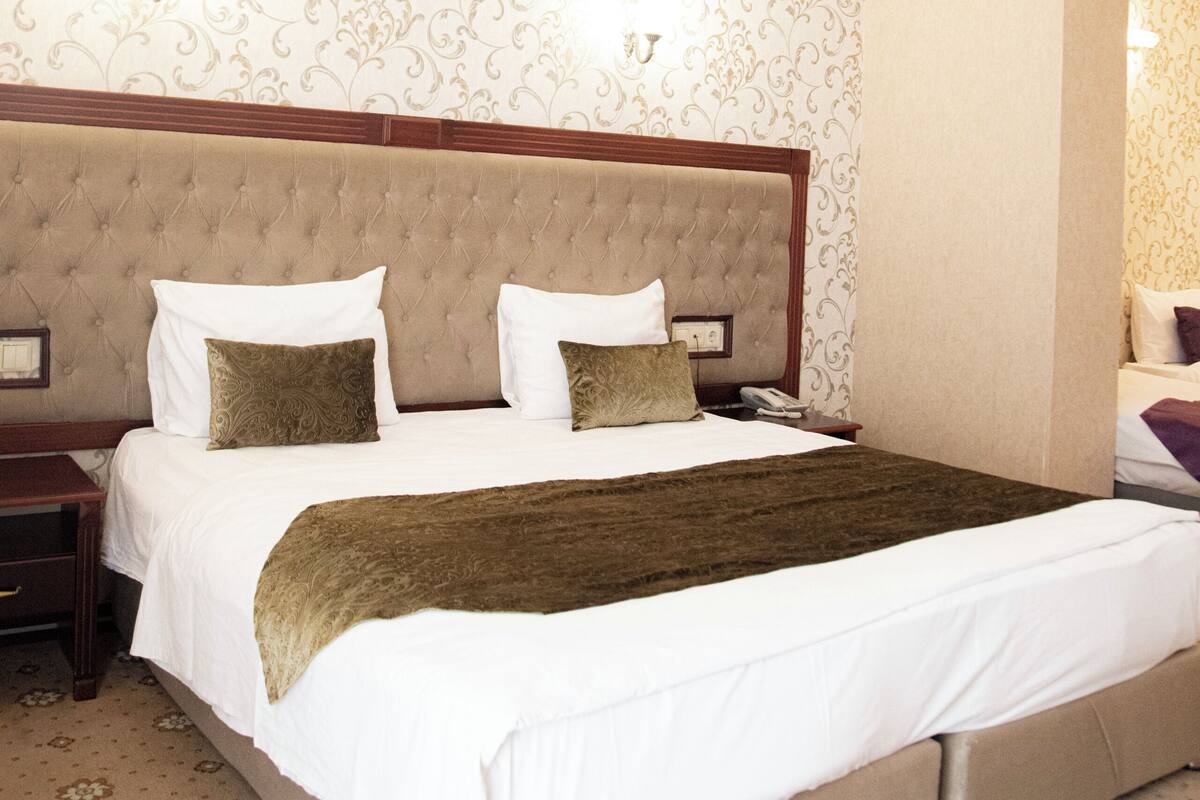 A hotel room with a large bed, a nightstand, and a wall-mounted lamp.