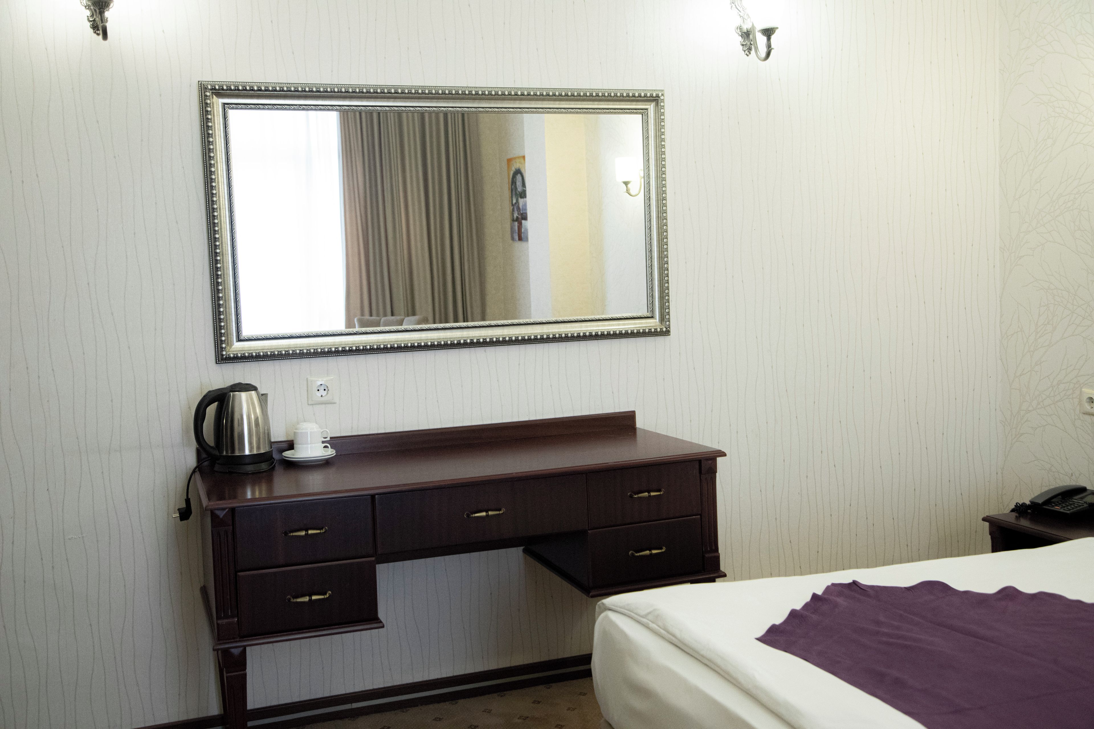 Quarto de hotel com cama, penteadeira com espelho, cafeteira e telefone.