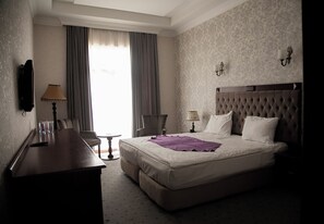 A hotel room with a bed, a desk, a chair, a lamp, and a window with curtains.