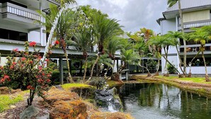 A hotel with a pool, surrounded by tropical plants and a small waterfall. - Hilo Lakefront Studio, Pool, Walk to Downtown (Hilo)