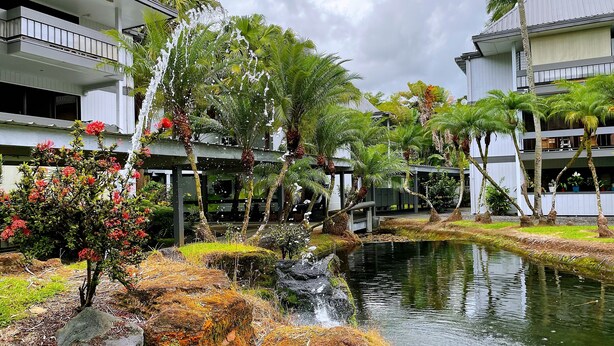 A hotel with a pool, surrounded by tropical plants and a small waterfall. - Hilo Lakefront Studio, Pool, Walk to Downtown (Hilo)
