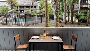 A dining area with a table set for two, overlooking a pool and a building with balconies. - Hilo Lakefront Studio, Pool, Walk to Downtown (Hilo)