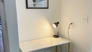 Ein kleiner, moderner Arbeitsraum mit einem weißen Marmor-Schreibtisch, einem schwarzen Bürostuhl, einem gerahmten abstrakten Gemälde an der Wand und einer Schreibtischlampe.