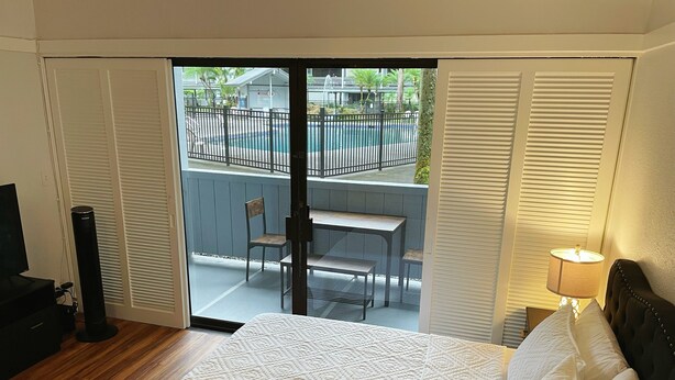 A hotel room with a bed, a desk, and a chair near a sliding glass door leading to a pool area. - Hilo Lakefront Studio, Pool, Walk to Downtown (Hilo)