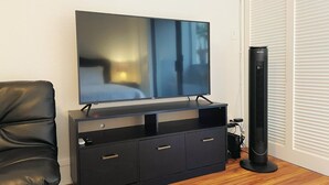 A modern living room with a flat-screen TV on a black entertainment unit, a leather sofa, and a standing heater. - Hilo Lakefront Studio, Pool, Walk to Downtown (Hilo)