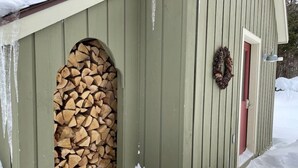 A wooden shed with a stack of firewood in an arched opening, a red door, and a wreath hanging on the wall. - Chalet at Mt Snow, ski-home, free shuttle (Dover)