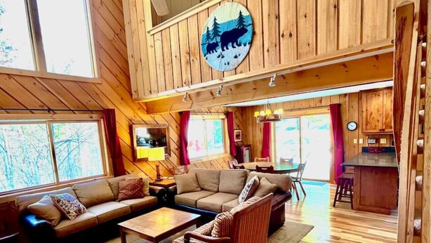 A spacious living area with a high ceiling, wooden walls, and a large window. - Chalet at Mt Snow, ski-home, free shuttle (Dover)