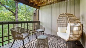 Un espacio de estar al aire libre cubierto con sillas de mimbre y una silla colgante, con vistas a un área boscosa.
